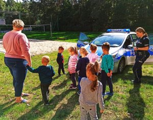 Zdjęcie przedstawia dzieci, które wraz z policjantką oglądają policyjny radiowóz.