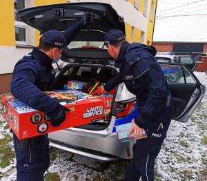 Zdjęcie przedstawia policjantów wyciągających prezenty z bagażnika radiowozu.