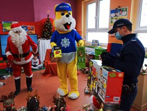 Zdjęcie przedstawia wręczanie dzieciom zabawek przez policjanta, obok Św. Mikołaj i maskotka opolskiej Policji &quot;Policuś&quot;