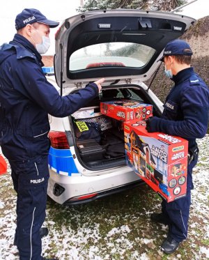 Zdjęcie przedstawia policjantów wyciagąjących zabawki z bagażnika radiowozu.