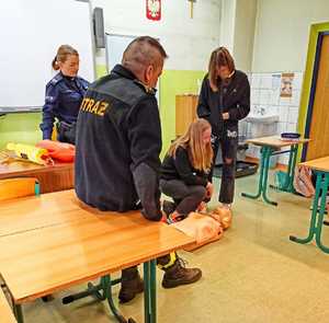 Zdjęcie przedstawia policjantkę oraz strażaka, którzy uczą młodzież pierwszej pomocy.