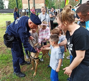 Zdjęcie przedstawia policjanta oraz dzieci, które głaszczą psa służbowego.