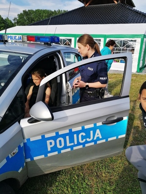 Zdjęcie przedstawia policjantkę, która pokazuje dziecku radiowóz.