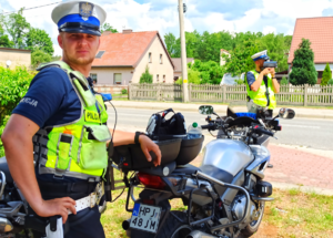 Zdjęcie przedstawia dwóch policjantów, jeden dokonuje pomiaru prędkości, drugi z nich stoi obok motocykla.