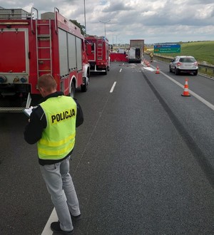 Zdjęcie przedstawia wypadek drogowy na autostradzie A4, na pierwszym planie policjant wykonujący oględziny.