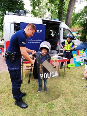 Zdjęcie przedstawia policjanta, obok którego stoi dziecko z tarczą z napisem &quot;Policja&quot;.