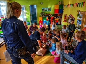 Zdjęcie przedstawia dzieci, które uczą się na fantomie pierwszej pomocy, obok strażak i policjantka.