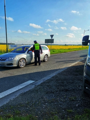 Zdjęcie przedstawia policjanta zatrzymującego kierującego pojazdem do kontroli drogowej.