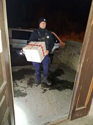 Zdjęcie przedstawia policjanta  przekazującego paczki żywnościowe potrzebującym.