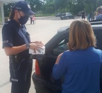 Policjantka wyciąga z pudełka maseczkę na parkingu przed marketem