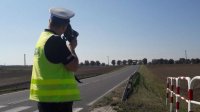 Policjant ruchu drogowego ubrany w odblaskową kamizelkę dokonuje pomiaru prędkości na drodze za pomocą ręcznego miernika prędkości.