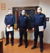 Zdjęcie przedstawia trzech policjantów na tle sztandaru: od lewej asp. sztab.S. Łyżwa, mł.insp. J. Roszczak, podkom. R. Gadomski