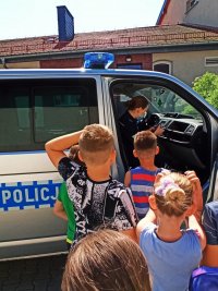 Zdjęcie przedstawia policjantkę prezentująca radiowóz policyjny dzieciom.