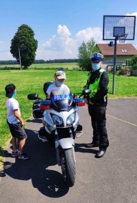 Zdjęcie przedstawia policjanta, prezentującego motocykl patrolu ruchu drogowego.