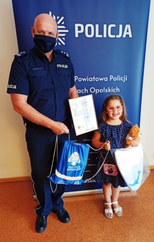 Zdjęcie przedstawia Komendanta Powiatowego Policji w Strzelcach Opolskich mł. insp. Jarosława Roszczaka z 5-latką, która odwiedziła strzelecka komendę.