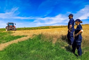 Zdjęcie przedstawia policjantów na polu, w tle widać traktor.