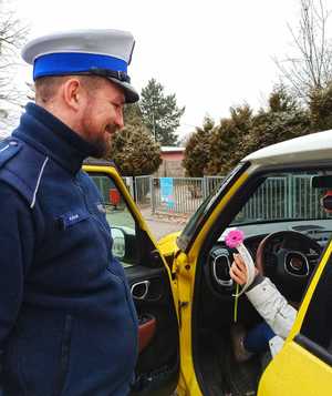 Zdjęcie przedstawia policjanta ruchu drogowego wręczającego kierującej kwiaty.