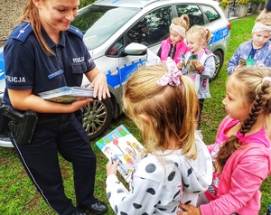 Zdjęcie przedstawia policjantkę rozdająca dzieciom materiały edukacyjne.