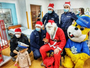 Zdjęcie przedstawia spotkanie policjantów, strażaka, Policusia i Mikołaja z dziećmi w szpitalu.