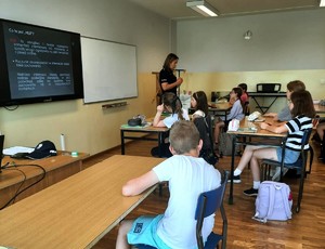 Zdjęcie kolorowe przedstawiającą policjantkę rozmawiającą z dziećmi w szkole.