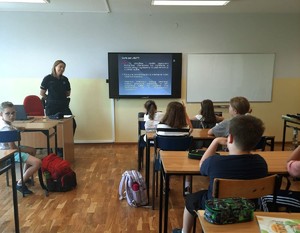 Zdjęcie kolorowe przedstawiającą policjantkę rozmawiającą z dziećmi w szkole.