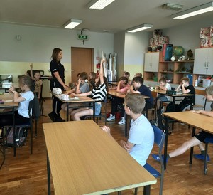 Zdjęcie kolorowe przedstawiającą policjantkę rozmawiającą z dziećmi w szkole.