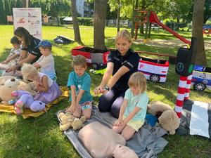 Zdjęcie kolorowe przedstawiające policjantki uczące dzieci przedszkolne pierwszej pomocy.