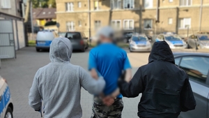 Zdjęcie kolorowe przedstawiającego policjantów prowadzących mężczyznę.