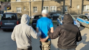 Zdjęcie kolorowe przedstawiającego policjantów prowadzących mężczyznę.