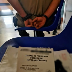 Zdjęcie kolorowe przedstawiające mężczyznę zakutego w kajdanki.