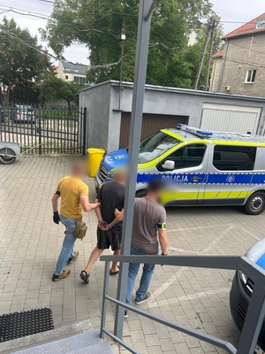 Zdjęcie kolorowe przedstawiające policjantów prowadzących zatrzymanego.