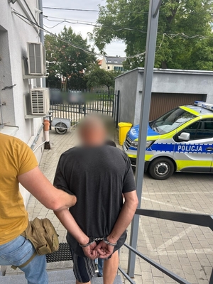 Zdjęcie kolorowe przedstawiające policjantów prowadzących zatrzymanego.