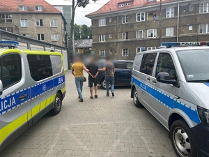 Zdjęcie kolorowe przedstawiające policjantów prowadzących zatrzymanego.