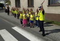Policjantka uczy dzieci prawidłowego przechodzenia po przejściu dla pieszych.
