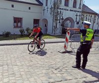 Zdjęcie przedstawia rowerzystę,k w trakcie wyścigu, w tle policjant zabezpieczający odcinek rajdu.