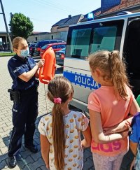 Zdjęcie przedstawia policjantkę,trzymającą boję ratunkową, prowadząca zajęcia z uczniami.