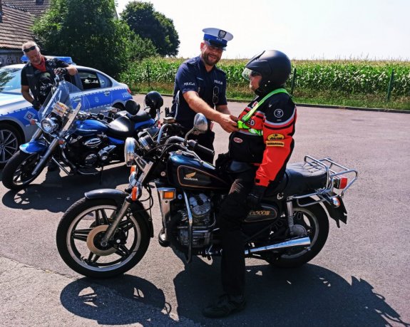 Zdjęcie przedstawia policjanta, który wręcza motocykliście szelki odblaskowe.