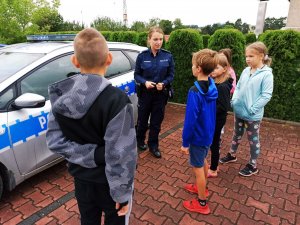 Zdjęcie przedstawia policjnatkę z dziećmi, w tle radiowóz.