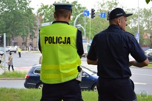 dwóch policjantów ruchu drogowego z oddali ogląda jak kieruje ruchem uczestnik konkursu